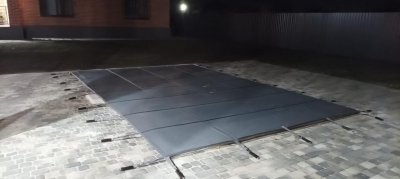 Прямоугольный бассейн с темно-срым защитным тентом на мощеной площадке ночью